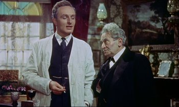 Movie still from “The Man Who Could Cheat Death” (1959), directed by Terence Fisher – A man in a suit and tie standing next to another man in a suit and tie; Medium shot, Low angle