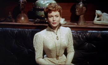 Movie still from “The Man Who Could Cheat Death” (1959), directed by Terence Fisher – A woman sitting on a couch wearing a white dress; Medium shot, High angle