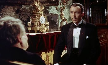 Movie still from “The Man Who Could Cheat Death” (1959), directed by Terence Fisher – A man in a tuxedo sitting in front of a clock; Medium shot, Over the shoulder angle