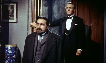 Movie still from “The Man Who Could Cheat Death” (1959), directed by Terence Fisher – A man in a suit and tie next to another man in a suit and tie; Medium shot, Over the shoulder angle