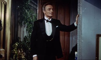 Movie still from “The Man Who Could Cheat Death” (1959), directed by Terence Fisher – A man in a tuxedo pointing at something on the wall; Medium shot, Low angle