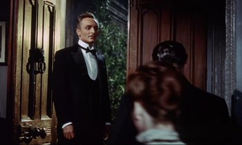 Movie still from “The Man Who Could Cheat Death” (1959), directed by Terence Fisher – A man in a tuxedo standing in front of two women; Medium shot, Low angle