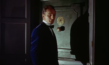Movie still from “The Man Who Could Cheat Death” (1959), directed by Terence Fisher – A man wearing a suit and bow tie standing in front of a door; Medium shot, Low angle