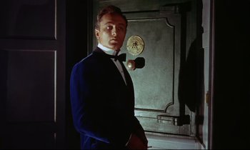 Movie still from “The Man Who Could Cheat Death” (1959), directed by Terence Fisher – A man in a blue suit standing in front of an antique safe; Medium shot, Low angle