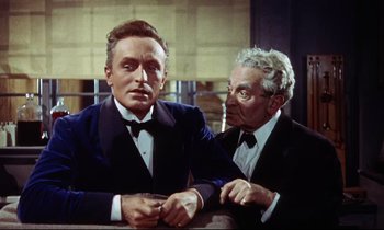 Movie still from “The Man Who Could Cheat Death” (1959), directed by Terence Fisher – A man in a suit and tie next to another man in a suit and tie; Medium shot, Over the shoulder angle