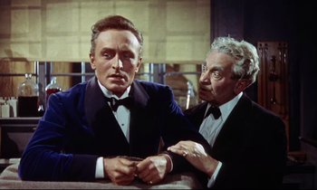 Movie still from “The Man Who Could Cheat Death” (1959), directed by Terence Fisher – A man in a suit and tie standing next to another man in a suit and tie; Medium shot, Over the shoulder angle