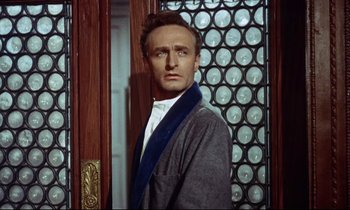 Movie still from “The Man Who Could Cheat Death” (1959), directed by Terence Fisher – A man standing in front of a door wearing a gray jacket; Close Up shot, Low angle