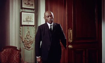 Movie still from “The Man Who Could Cheat Death” (1959), directed by Terence Fisher – An older man wearing a suit and tie in front of a door; Medium shot, Low angle