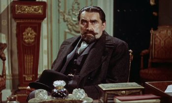 Movie still from “The Man Who Could Cheat Death” (1959), directed by Terence Fisher – A man sitting at a table in a suit and tie; Medium shot, Over the shoulder angle