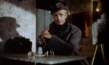 Movie still from “The Man Who Could Cheat Death” (1959), directed by Terence Fisher – A man sitting at a table in a room; Medium shot, Low angle
