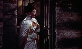Movie still from “The Man Who Could Cheat Death” (1959), directed by Terence Fisher – A woman in a long white dress standing in front of a door; Medium shot, Low angle