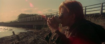 Movie still from “The Man Who Fell to Earth” (1976), directed by Nicolas Roeg – A woman drinking a cup of coffee near a bridge; Medium shot, Over the shoulder angle