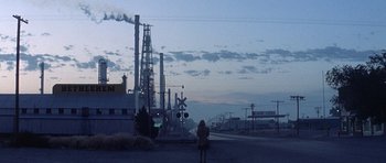 Movie still from “The Man Who Fell to Earth” (1976), directed by Nicolas Roeg – A woman standing on the side of a road near a train station; Extreme Wide shot, High angle
