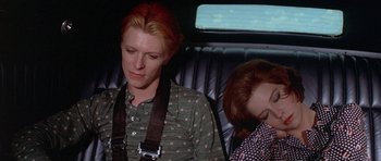 Movie still from “The Man Who Fell to Earth” (1976), directed by Nicolas Roeg – A man and a woman sitting in the back of a car; Medium shot, High angle