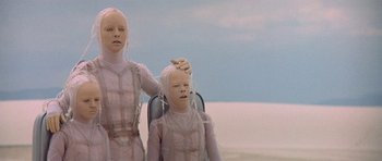 Movie still from “The Man Who Fell to Earth” (1976), directed by Nicolas Roeg – Two people in pink suits are sitting in a chair; Close Up shot, Low angle