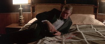 Movie still from “The Man Who Fell to Earth” (1976), directed by Nicolas Roeg – A man in a suit playing cards on a bed; Medium shot, Low angle