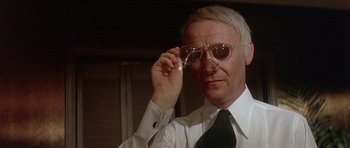Movie still from “The Man Who Fell to Earth” (1976), directed by Nicolas Roeg – An older man in a white dress shirt and tie holding a pair of glasses; Close Up shot, Low angle
