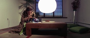 Movie still from “The Man Who Fell to Earth” (1976), directed by Nicolas Roeg – A person sitting at a table with a camera; Wide shot, Low angle