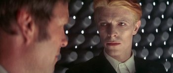 Movie still from “The Man Who Fell to Earth” (1976), directed by Nicolas Roeg – A person in a suit looking at another person; Close Up shot, Over the shoulder angle