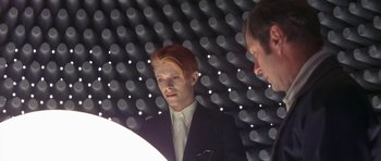 Movie still from “The Man Who Fell to Earth” (1976), directed by Nicolas Roeg – A man in a black suit and white shirt; Medium shot, Over the shoulder angle