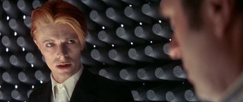 Movie still from “The Man Who Fell to Earth” (1976), directed by Nicolas Roeg – A man with blonde hair and a black suit; Close Up shot, Over the shoulder angle