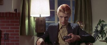 Movie still from “The Man Who Fell to Earth” (1976), directed by Nicolas Roeg – A man in a black suit holding a camera; Close Up shot, Over the shoulder angle