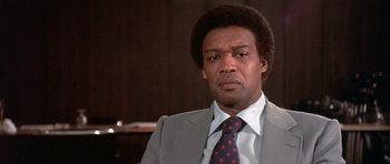 Movie still from “The Man Who Fell to Earth” (1976), directed by Nicolas Roeg – A man wearing a suit and tie in front of a wooden wall; Close Up shot, Low angle