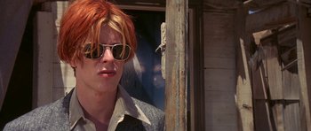 Movie still from “The Man Who Fell to Earth” (1976), directed by Nicolas Roeg – A man with red hair wearing sunglasses and standing next to a wooden pole; Close Up shot, Low angle