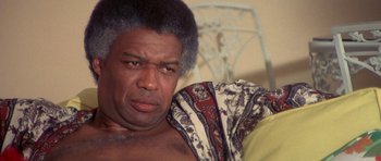 Movie still from “The Man Who Fell to Earth” (1976), directed by Nicolas Roeg – An older man with a beard is sitting on a couch; Close Up shot, Low angle