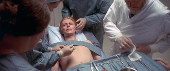 Movie still from “The Man Who Fell to Earth” (1976), directed by Nicolas Roeg – A woman is being examined by doctors in an operating room; Medium shot, Overhead angle