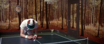 Movie still from “The Man Who Fell to Earth” (1976), directed by Nicolas Roeg – A man is playing ping pong in a room with trees; Wide shot, Overhead angle