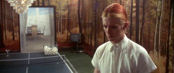 Movie still from “The Man Who Fell to Earth” (1976), directed by Nicolas Roeg – A man in a white shirt is standing in front of a tv; Medium shot, Over the shoulder angle
