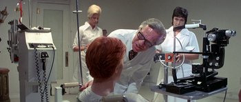 Movie still from “The Man Who Fell to Earth” (1976), directed by Nicolas Roeg – An older man in a white lab coat talking to a young woman; Medium shot, Over the shoulder angle