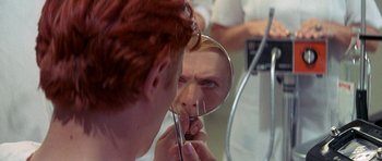 Movie still from “The Man Who Fell to Earth” (1976), directed by Nicolas Roeg – A woman looking into a mirror while holding a pair of scissors; Extreme Close Up shot, Over the shoulder angle