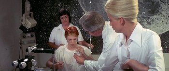 Movie still from “The Man Who Fell to Earth” (1976), directed by Nicolas Roeg – A group of people standing around a woman in a room; Medium shot, High angle