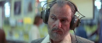 Movie still from “The Man Who Fell to Earth” (1976), directed by Nicolas Roeg – An older man with a gray beard wearing headphones; Close Up shot, Low angle