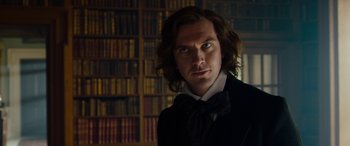 Movie still from “The Man Who Invented Christmas” (2017), directed by Bharat Nalluri – A man with long hair wearing a suit and bow tie; Close Up shot, Over the shoulder angle