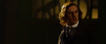 Movie still from “The Man Who Invented Christmas” (2017), directed by Bharat Nalluri – A man with long blonde curly hair wearing a suit and tie; Close Up shot, Over the shoulder angle