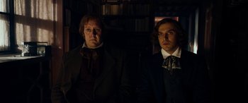 Movie still from “The Man Who Invented Christmas” (2017), directed by Bharat Nalluri – Two men standing next to each other in a dark room; Medium shot, Low angle