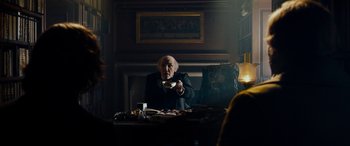 Movie still from “The Man Who Invented Christmas” (2017), directed by Bharat Nalluri – An old man sitting at a table in a dark room; Medium shot, Over the shoulder angle