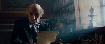 Movie still from “The Man Who Invented Christmas” (2017), directed by Bharat Nalluri – An old man sitting in a chair looking at a paper; Close Up shot, Over the shoulder angle