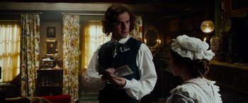 Movie still from “The Man Who Invented Christmas” (2017), directed by Bharat Nalluri – A man in a vest and tie holding a book in his hands; Medium shot, Over the shoulder angle