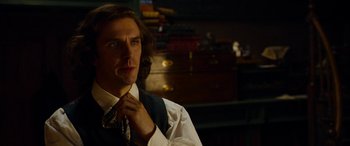 Movie still from “The Man Who Invented Christmas” (2017), directed by Bharat Nalluri – A man with long brown hair wearing a white shirt and a tie; Close Up shot, Over the shoulder angle