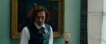 Movie still from “The Man Who Invented Christmas” (2017), directed by Bharat Nalluri – A man in a vest and tie standing in front of an oil lamp; Medium shot, Over the shoulder angle