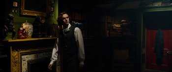 Movie still from “The Man Who Invented Christmas” (2017), directed by Bharat Nalluri – A man standing in a dark room wearing a white shirt; Medium shot, Low angle