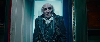 Movie still from “The Man Who Invented Christmas” (2017), directed by Bharat Nalluri – An old man wearing chains and wearing a suit; Medium shot, Low angle