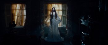 Movie still from “The Man Who Invented Christmas” (2017), directed by Bharat Nalluri – A woman in a white dress standing in front of a window; Wide shot, Low angle