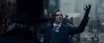 Movie still from “The Man Who Invented Christmas” (2017), directed by Bharat Nalluri – A man in a suit and tie standing in front of a group of people; Medium shot, Low angle