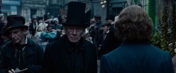 Movie still from “The Man Who Invented Christmas” (2017), directed by Bharat Nalluri – An old man wearing a top hat in the middle of a crowd; Medium shot, Over the shoulder angle
