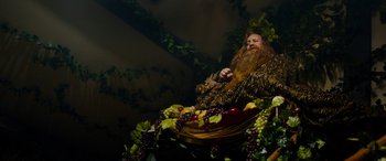 Movie still from “The Man Who Invented Christmas” (2017), directed by Bharat Nalluri – A man with a beard sitting in a basket of fruit; Wide shot, Low angle